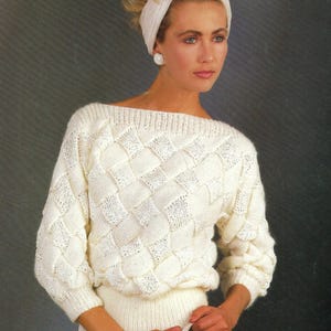 Könnte beinhalten: Ein weißer Strickpullover mit einem Zopfmuster. Der Pullover hat einen Boot Ausschnitt und lange Ärmel.