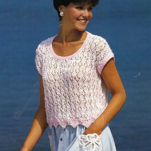 May include: A pink crocheted top with a scalloped hem and short sleeves. The top is worn over a light blue skirt with a white lace pocket.