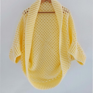 May include: A yellow crocheted cardigan with a wide, open neckline and short sleeves. The cardigan is made with a delicate, open stitch pattern.