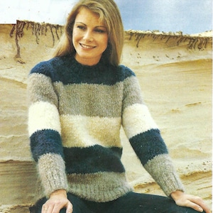 May include: A striped jumper with long sleeves in shades of grey, white, and blue. The jumper has a crew neck and is made of a soft, fuzzy yarn.