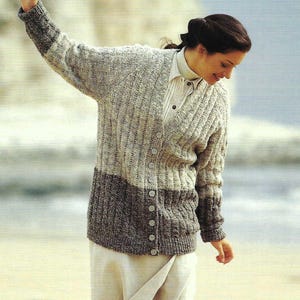 May include: A two-tone gray cardigan sweater with a button-up front. The top half is light gray, and the bottom half is dark gray. The sleeves have dark gray cuffs. The sweater is worn over a white collared shirt and a beige skirt.