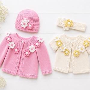 Può includere: Un cardigan in maglia rosa a maniche lunghe con fiori all'uncinetto bianchi e rosa, un berretto in maglia rosa abbinato con due fiori, un cardigan in maglia color crema a maniche corte con fiori gialli e una fascia in maglia color crema.