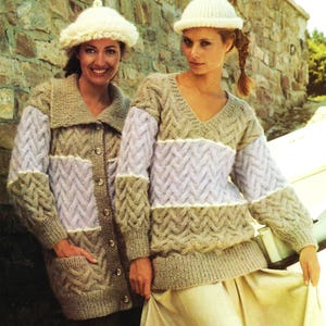 May include: Two women wearing knitted sweaters with a cable knit pattern. The sweaters are in shades of brown and purple. The women are wearing white knit hats.