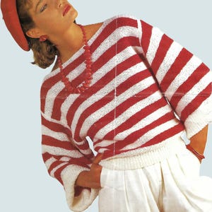 Könnte beinhalten: Ein rot-weiß gestreifter Pullover mit passendem rotem Hut und Schmuck. Der Pullover hat breite horizontale Streifen und Dreiviertelärmel. Das Model trägt auch eine weiße Hose und rote Accessoires.