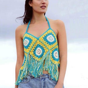 May include: A crocheted halter top with a geometric pattern in yellow, blue, and white. The top has a fringe trim.