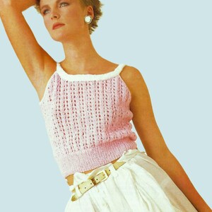 May include: A pink crocheted tank top with white trim and thin straps. The top is worn with a white skirt and a gold belt.