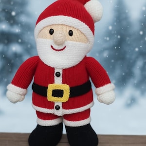 May include: A knitted Santa Claus doll with a red suit, hat, and black boots. The doll has a white beard, mustache, and trim, with a black belt and a gold buckle. The background is a blurred winter scene.