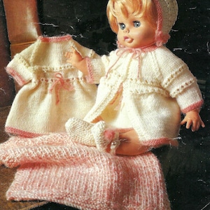 Può includere: Un set di abiti in maglia per bambole in bianco e rosa. Il set comprende un vestito, un cardigan, un cappello e scarpette. L'abito è progettato per una bambola di circa 30 cm.