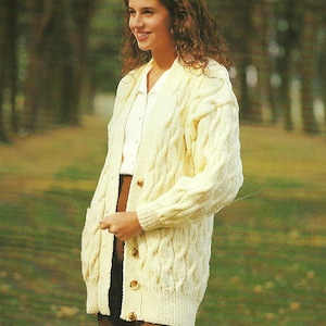 May include: A white cable knit cardigan with a button closure and pockets. The cardigan is worn by a person with long brown hair.