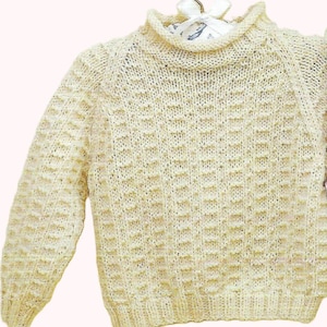 May include: A cream knitted jumper with a high neck and long sleeves. The jumper has a waffle stitch pattern.