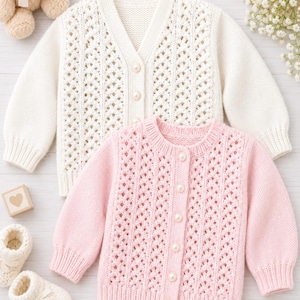 May include: Two long-sleeved knit cardigans, one in cream and one in light pink, featuring a vertical openwork pattern, ribbed cuffs and hems, and round pearl-like buttons down the front. The garments are displayed alongside a small teddy bear.