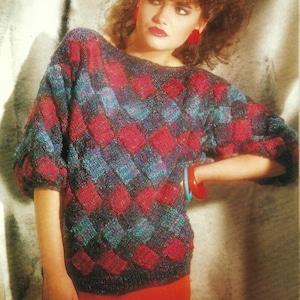 Pode incluir: Uma mulher vestindo um suéter xadrez vermelho e azul com uma saia vermelha. Ela está usando brincos vermelhos e tem o cabelo penteado em um grande bouffant.