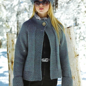 Puede incluir: Chaqueta de punto azul con gorro y gafas de sol a juego. La chaqueta tiene un patrón texturizado y un cierre de un solo botón. Los puños están doblados. El fondo es una escena invernal nevada.