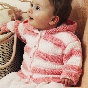 Op de afbeelding: Een roze en wit gestreepte gebreide babytrui met een capuchon. De trui heeft een knoopsluiting en is gemaakt van zacht, getextureerd garen.