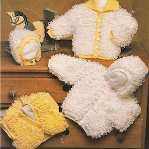 Könnte beinhalten: Vier gestrickte Babysweater in Weiß und Gelb. Die Pullover sind aus einem flauschigen, strukturierten Garn gefertigt. Zwei der Pullover haben Kapuzen.