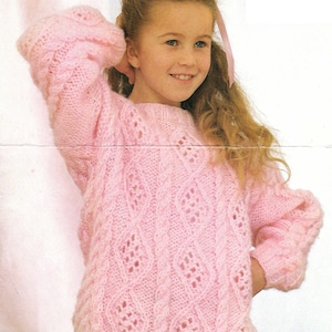 Könnte beinhalten: Ein rosa gestrickter Pullover mit einem Zopfmuster und einem zarten Spitzenmuster. Der Pullover hat lange Ärmel und einen runden Ausschnitt.