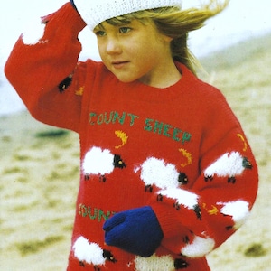 May include: A red knitted sweater with a white knitted hat and blue knitted gloves. The sweater has a white sheep design and the text "County Sheep" on the front.