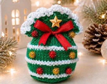 May include: A green crocheted drawstring pouch featuring white horizontal stripes, a red ribbon bow, a gold star embellishment, and small red and gold pom-poms. The pouch has a scalloped white crocheted top edge and a rounded base shape.