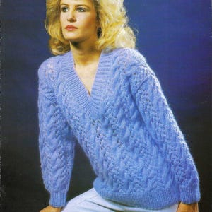 Può includere: Un maglione di lana blu chiaro con scollo a V e un motivo a treccia.