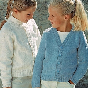 May include: Two girls wearing knitted cardigans. The girl on the left is wearing a white cardigan with a button closure. The girl on the right is wearing a light blue cardigan with a button closure.
