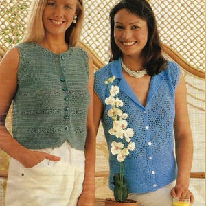 May include: Two women wearing crocheted sleeveless tops. The woman on the left is wearing a blue-green top with buttons down the front. The woman on the right is wearing a light blue top with buttons down the front. Both women are wearing white trousers.