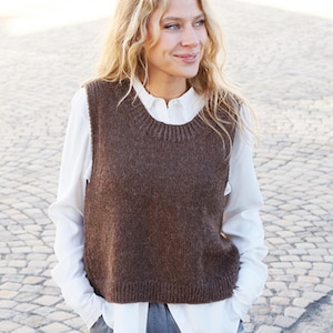 Puede incluir: Un chaleco de punto marrón con cuello redondo. El chaleco se lleva sobre una camisa blanca abotonada.