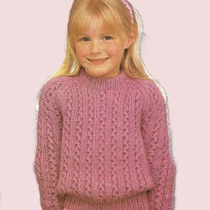 May include: A pink knitted jumper with a delicate openwork pattern. The jumper has a round neckline and long sleeves.