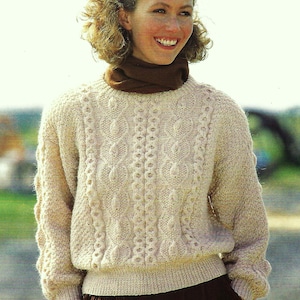 Può includere: Un maglione di colore crema lavorato a maglia con un motivo a treccia. Il maglione ha un collo rotondo e maniche lunghe.