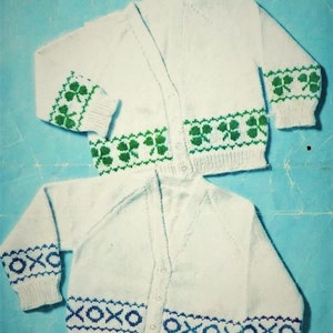 Puede incluir: Dos cárdigans de punto blanco con ribetes de diferentes colores. Un cárdigan tiene un ribete de trébol verde y el otro tiene un ribete azul y blanco. El texto "4-PLY NYLON" y "6 meses a 3 años" está impreso en la página.