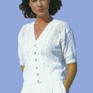 May include: A white knitted cardigan with a V-neck and button fastening. The short-sleeved top has a textured design on the front and sleeves. The model is wearing a matching white outfit against a light blue background.