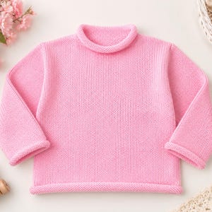 Könnte beinhalten: Ein einfarbiger, hellrosa Langarmpullover mit Stehkragen, langen Ärmeln mit gerollten Bündchen und einem gerollten Saum. Das Kleidungsstück ist durchgehend mit einer gleichmäßigen Strickstruktur auf der Vorder- und Rückseite gefertigt.