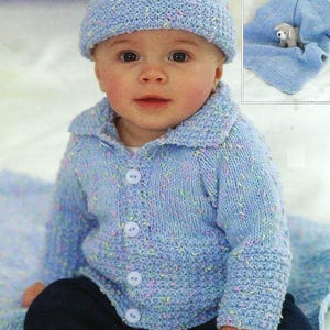 May include: A baby wearing a blue knitted cardigan with buttons, a matching blue knitted hat, and blue jeans. The cardigan and hat have a speckled pattern with light blue, pink, and green flecks.