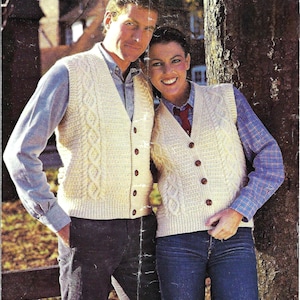 Puede incluir: Un par de chalecos de punto de color crema con un patrón de punto de cable y cierres de botón. Los chalecos los llevan dos personas de pie una al lado de la otra.