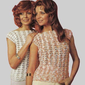 May include: Two women wearing crochet tops. One top is white, the other is peach and white. Both tops have a floral pattern and short sleeves. The women are smiling and wearing gold bracelets.