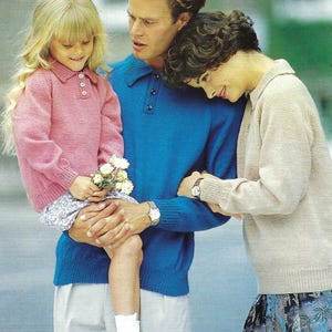 May include: A family portrait featuring a young girl in a pink collared sweater, held by a man in a blue polo shirt. The woman wears a beige sweater. The girl holds flowers and wears black patent leather shoes.