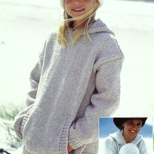 Op de afbeelding: Een lichtgrijze hoodie met een zak op de voorkant. De trui is gemaakt van een zachte, gebreide stof. Het model draagt een witte gebreide muts.