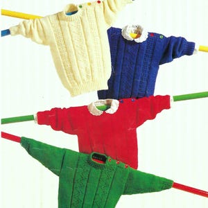 Op de afbeelding: Vier kleurrijke gebreide truien worden getoond. De truien zijn crème, blauw, rood en groen. Elke trui heeft een uniek ontwerp, met kabelbreiwerk en decoratieve knopen. Een speelgoedtrein staat bovenop de bovenste trui.