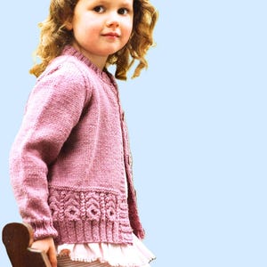 May include: A pink knitted cardigan with a button closure and a decorative stitch pattern around the bottom hem.