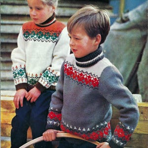 Op de afbeelding: Twee kinderen dragen kleurrijke gebreide truien met een traditioneel Scandinavisch patroon. Het meisje draagt een witte trui met oranje, groene en witte strepen, en de jongen draagt een grijze trui met rode, witte en grijze strepen.
