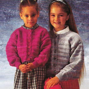 May include: Two girls wearing knitted cardigans. The girl on the left is wearing a pink cardigan with buttons and a plaid skirt. The girl on the right is wearing a gray cardigan with buttons and a red skirt.