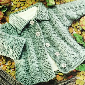 May include: A green knitted baby cardigan with a cable knit pattern and button closure.