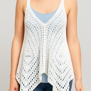 May include: A white, open-weave crochet tank top with a V-neck design. The top has wide straps and a flowing, asymmetrical hemline. Worn over a light blue top and paired with blue jeans.