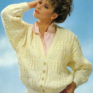 Peut inclure: Cardigan en tricot crème texturé avec un col en V et une fermeture boutonnée. Le pull à manches longues présente un ourlet et des poignets côtelés. La femme porte une chemise rose à col en dessous. Le fond est un dégradé de bleu et de blanc.