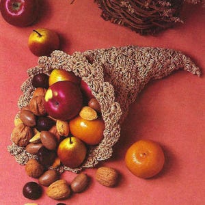 May include: A crocheted cornucopia filled with apples, pears, oranges, and nuts. The cornucopia is spilling its contents onto a red surface.