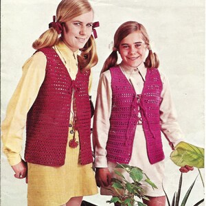 May include: Two young people wearing matching burgundy crochet vests with a lace-up front. They are also wearing collared shirts and skirts. The image has a vintage aesthetic, with a warm color palette and soft lighting.