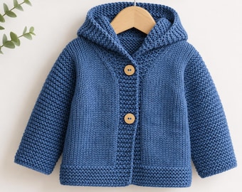 May include: A blue knitted hooded cardigan featuring a textured garter stitch pattern throughout the body and sleeves. The garment includes a hood, long sleeves, and a front closure secured by two round, light-colored wooden buttons.
