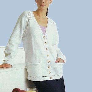 Puede incluir: Un cárdigan blanco de punto con cuello en V, mangas largas y cierre de botones. El cárdigan tiene bolsillos en la parte delantera y un delicado ribete de encaje alrededor del cuello y los puños.