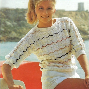 May include: A woman wearing a white, brown and black striped knitted sweater with a wavy pattern. She is sitting on a red boat and wearing sunglasses.