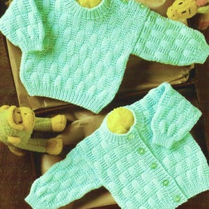 May include: Two knitted baby sweaters in a light blue colour. One sweater has a crew neck and the other has a button-up front.