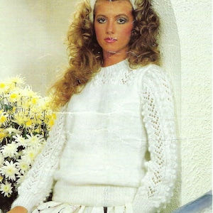 May include: A white knitted sweater with a delicate lace pattern on the sleeves and a white headband. The sweater has a round neckline and a slightly fitted silhouette.